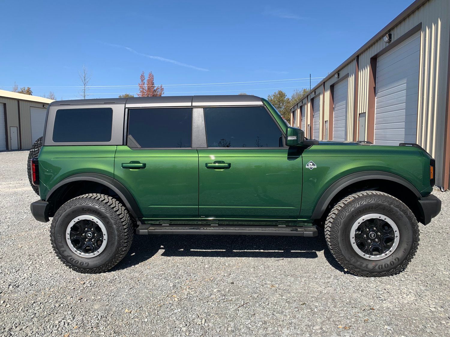 Green Ford Bronco parked next to storage units on a gravel surface under a blue sky.
