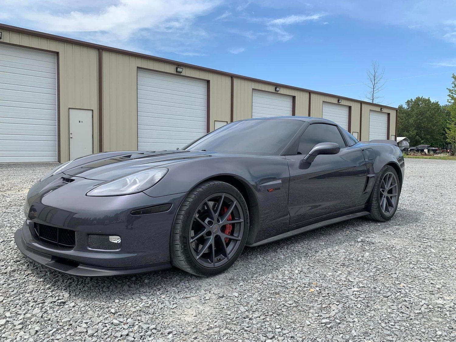 Dark gray Chevrolet Corvette sports car parked on gravel, with red brake calipers visible.