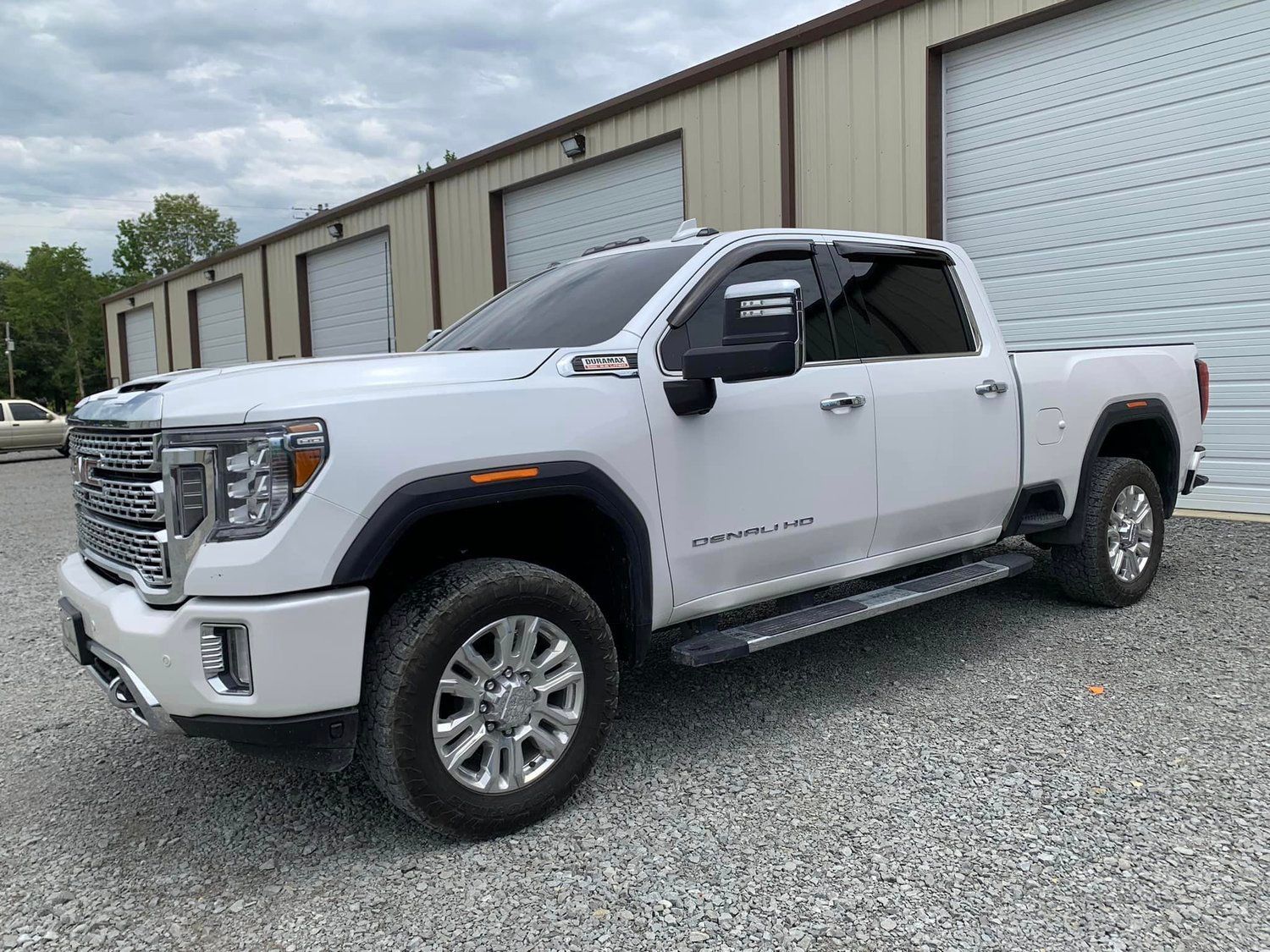 White GMC Sierra pickup truck parked on gravel in front of a building with garage doors.