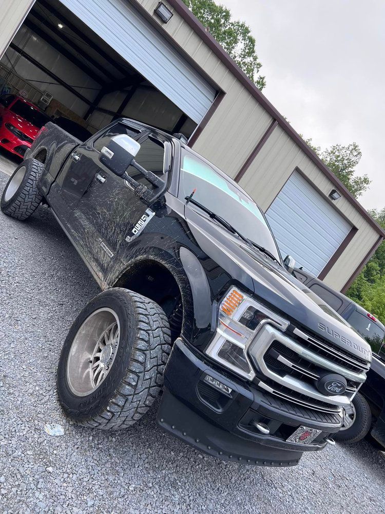 Black Ford pickup truck parked in front of a metal building with the door open.