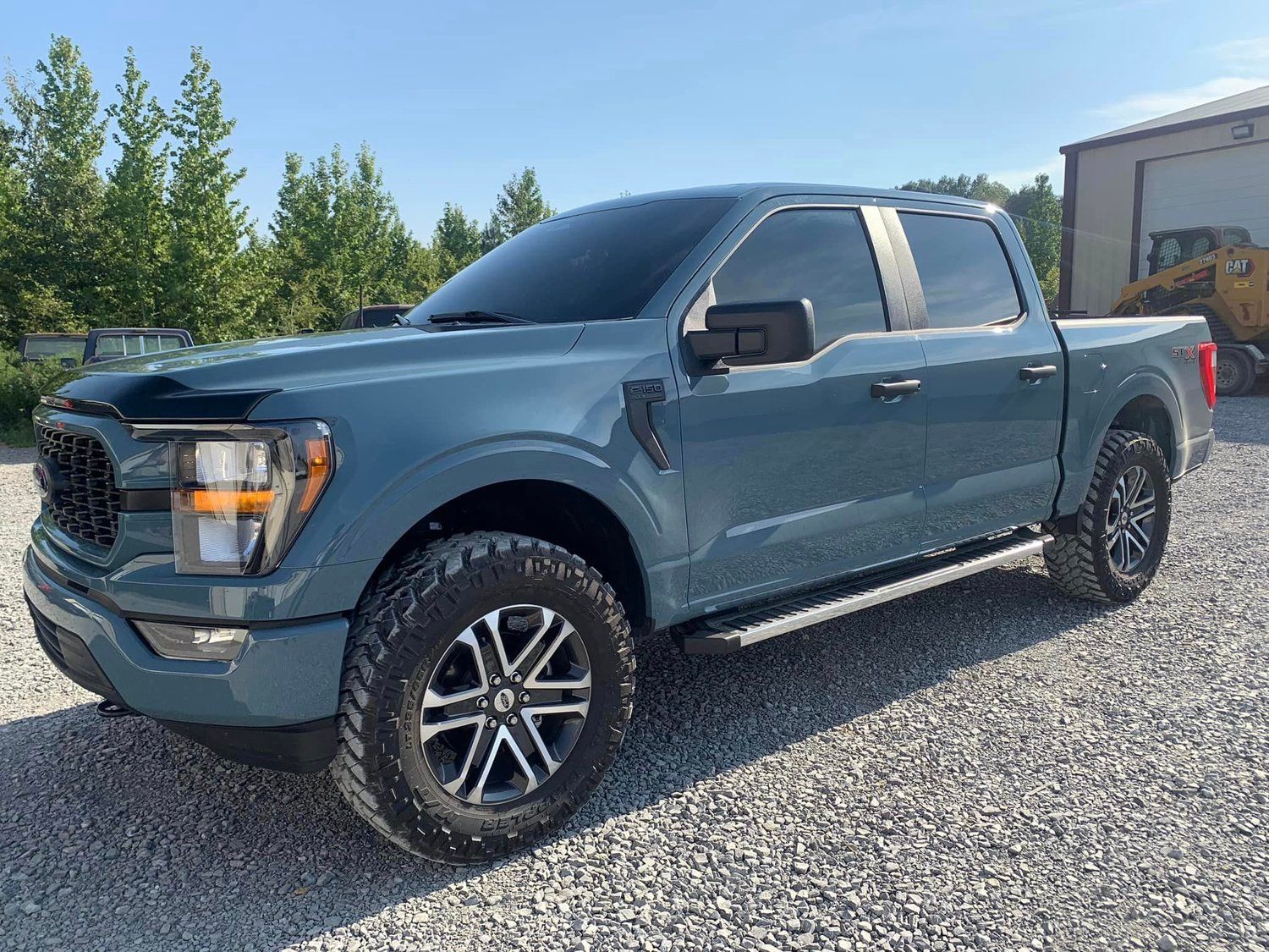Blue Ford F-150 truck parked on gravel. It has dark tinted windows and black accents.