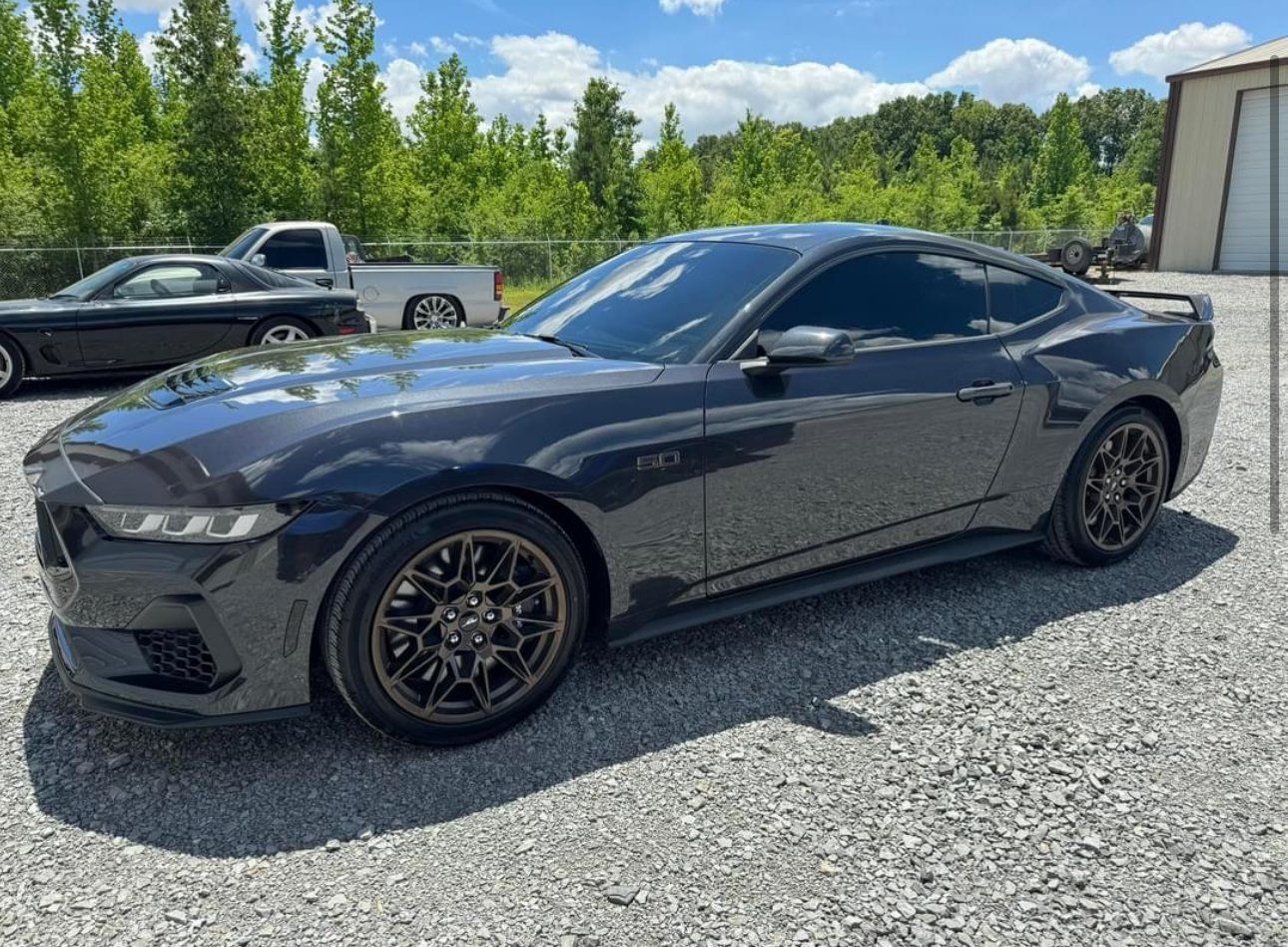 Dark gray Ford Mustang with tinted windows, parked on gravel.