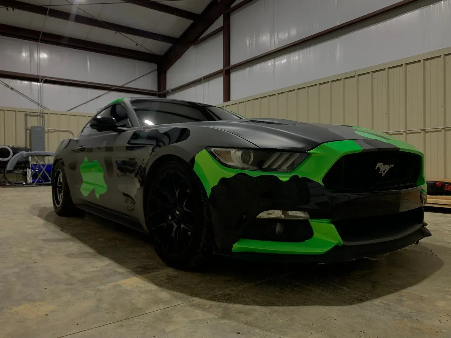Black Ford Mustang with green accents inside a garage.