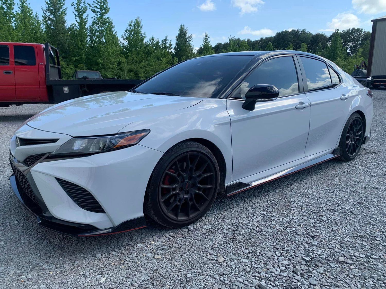 White Toyota Camry with black accents parked on gravel.