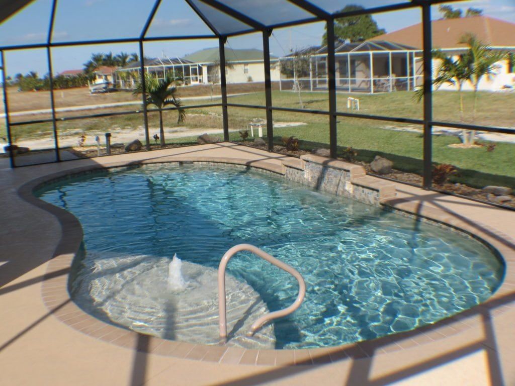 Pool enclosed by a screen with waterfall and fountain, surrounded by patio, lawn, and houses.