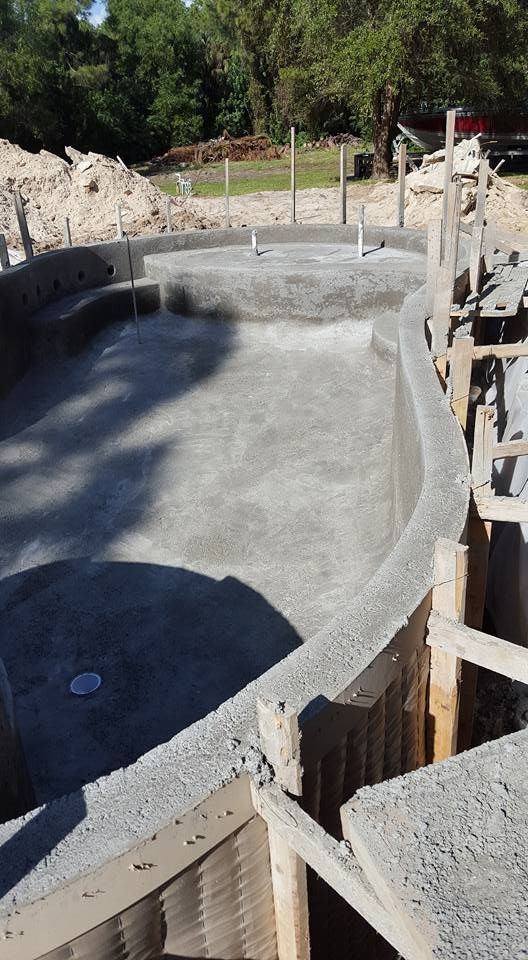 Concrete pool under construction, surrounded by wooden framing, outdoors on a sunny day.