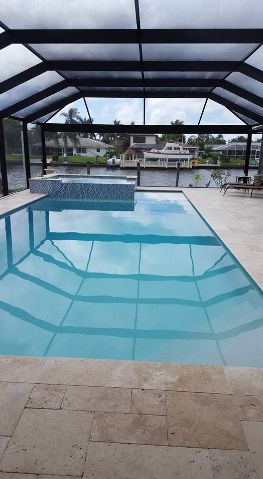 Pool with water reflecting sky under a screened enclosure. Houses and waterway visible in the background.