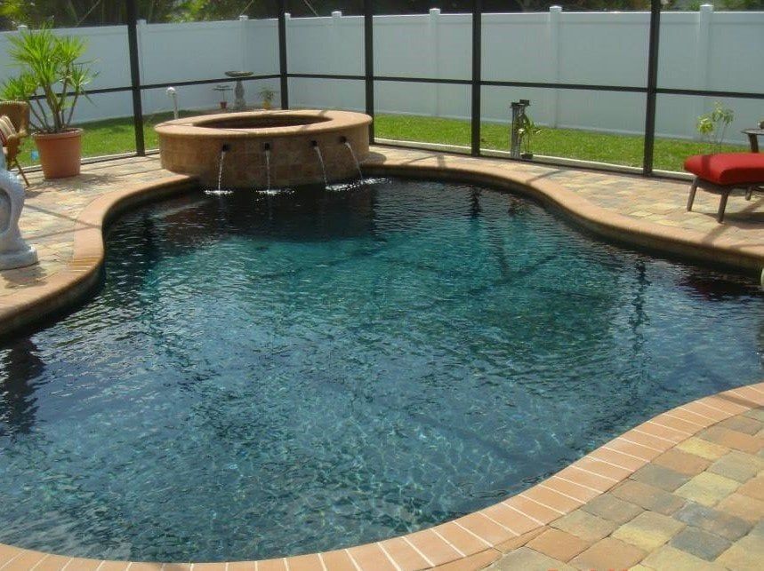 Swimming pool with a circular water feature, surrounded by brick and enclosed by a screened fence.