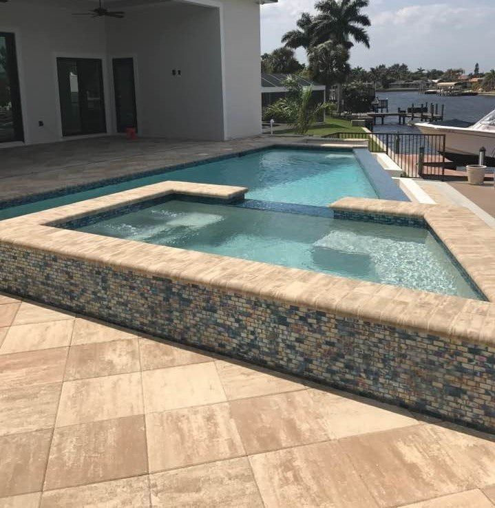 Pool with a spa area next to a house, and water view. Tan and blue tiles.