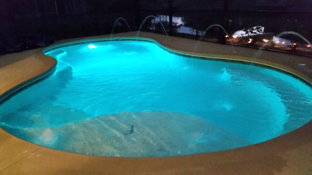 Pool with blue lights at night, water fountains spraying, beige border.