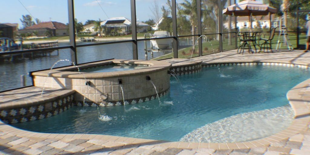 A pool with a jacuzzi, jets, and a gazebo overlooking a canal.