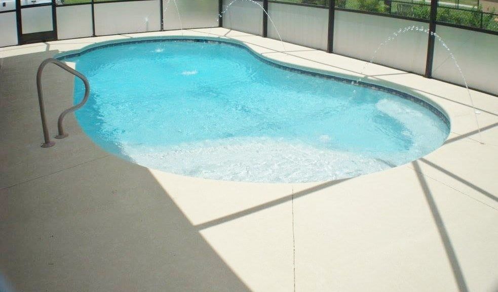 Pool with clear blue water, surrounded by light-colored concrete and a screened enclosure.