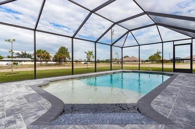 Pool enclosure with a swimming pool surrounded by gray paving stones, under a blue sky.