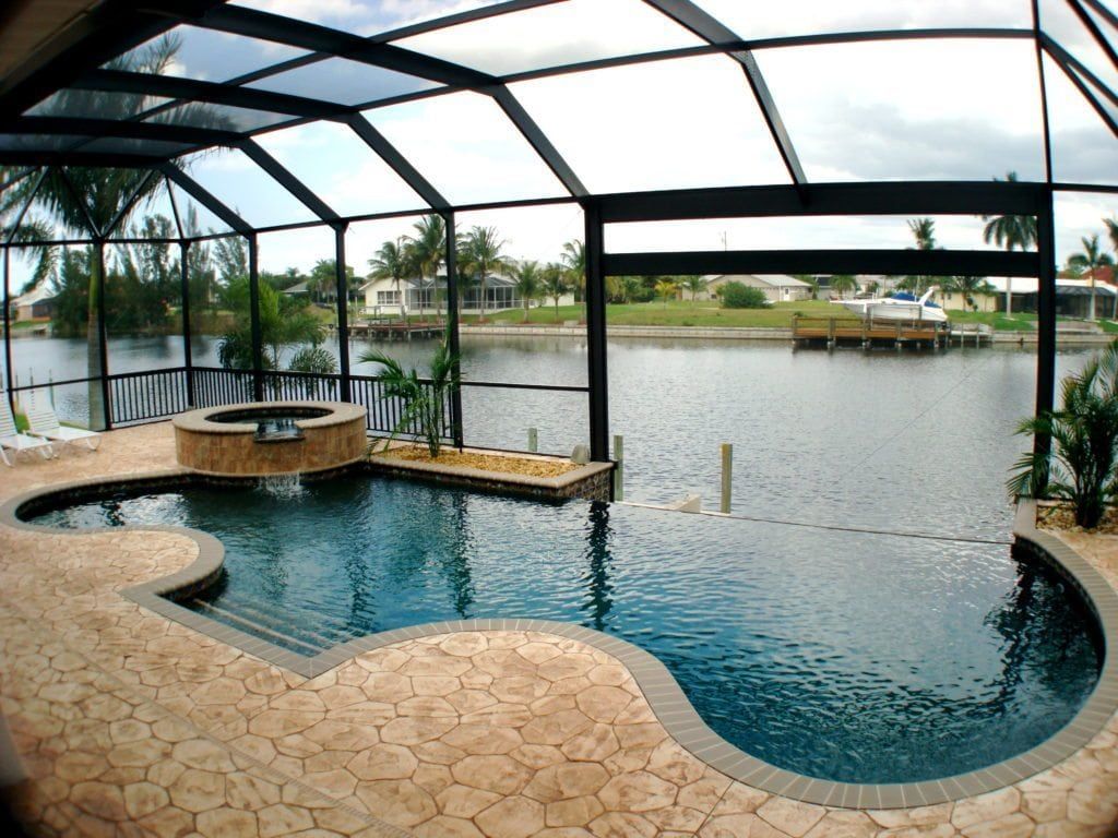 Pool enclosed by a screen with a water view; the pool has a jacuzzi and is surrounded by stone.
