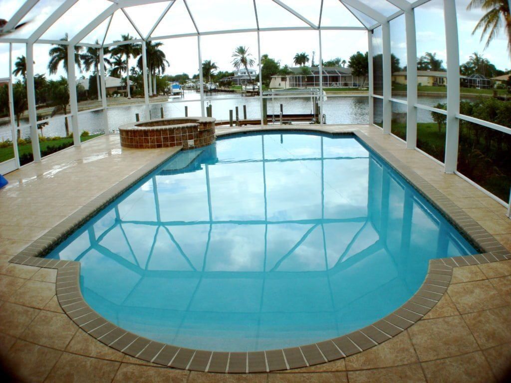 Pool with clear blue water inside a screened-in patio, canal and houses visible in the background.