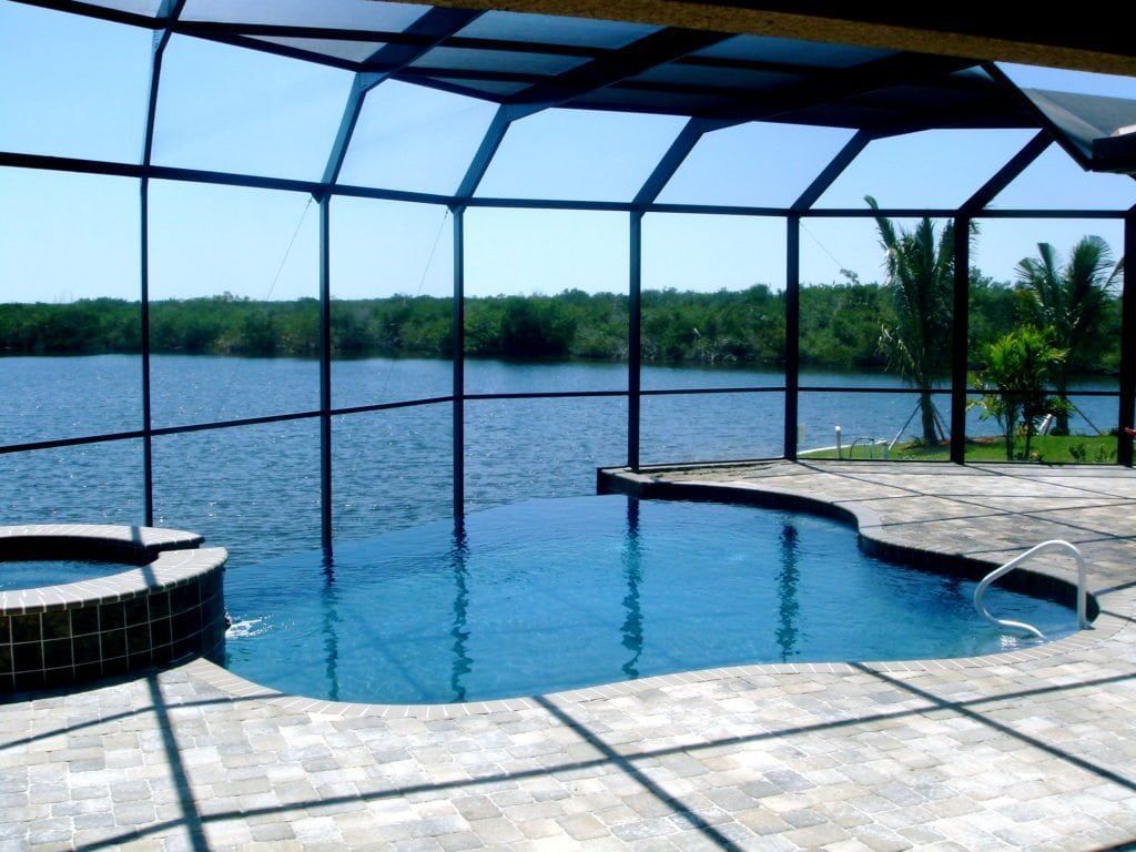 Pool with waterfront view, enclosed by screened patio; blue water and sky, stone patio.