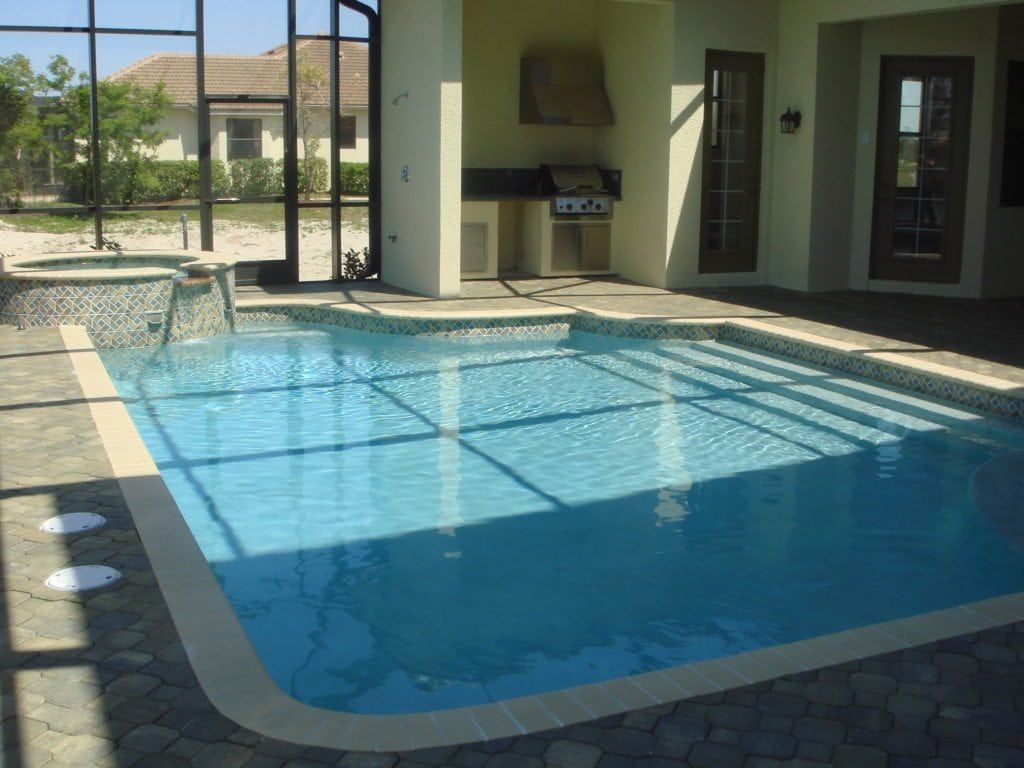 Outdoor pool with blue water and attached hot tub; a grill and covered patio are nearby.