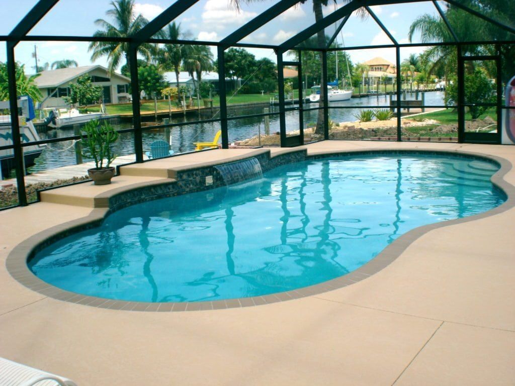 Swimming pool with waterfall feature, surrounded by a screened enclosure, canal backdrop.