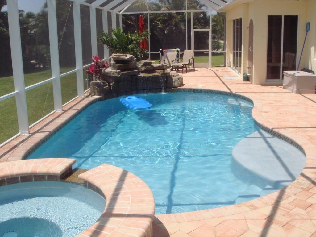 Enclosed backyard pool with waterfall feature, spa, and surrounding brick patio.