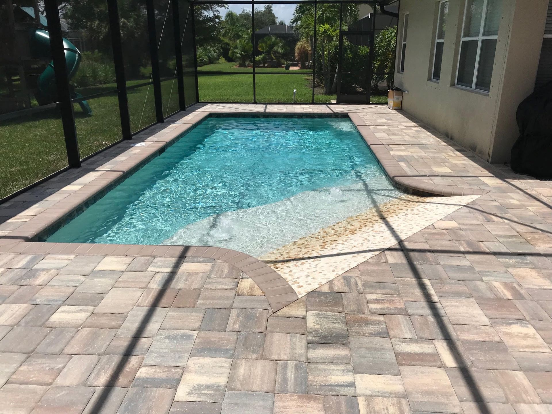 A small rectangular pool with a shallow end, surrounded by stone pavers, with a screened enclosure.