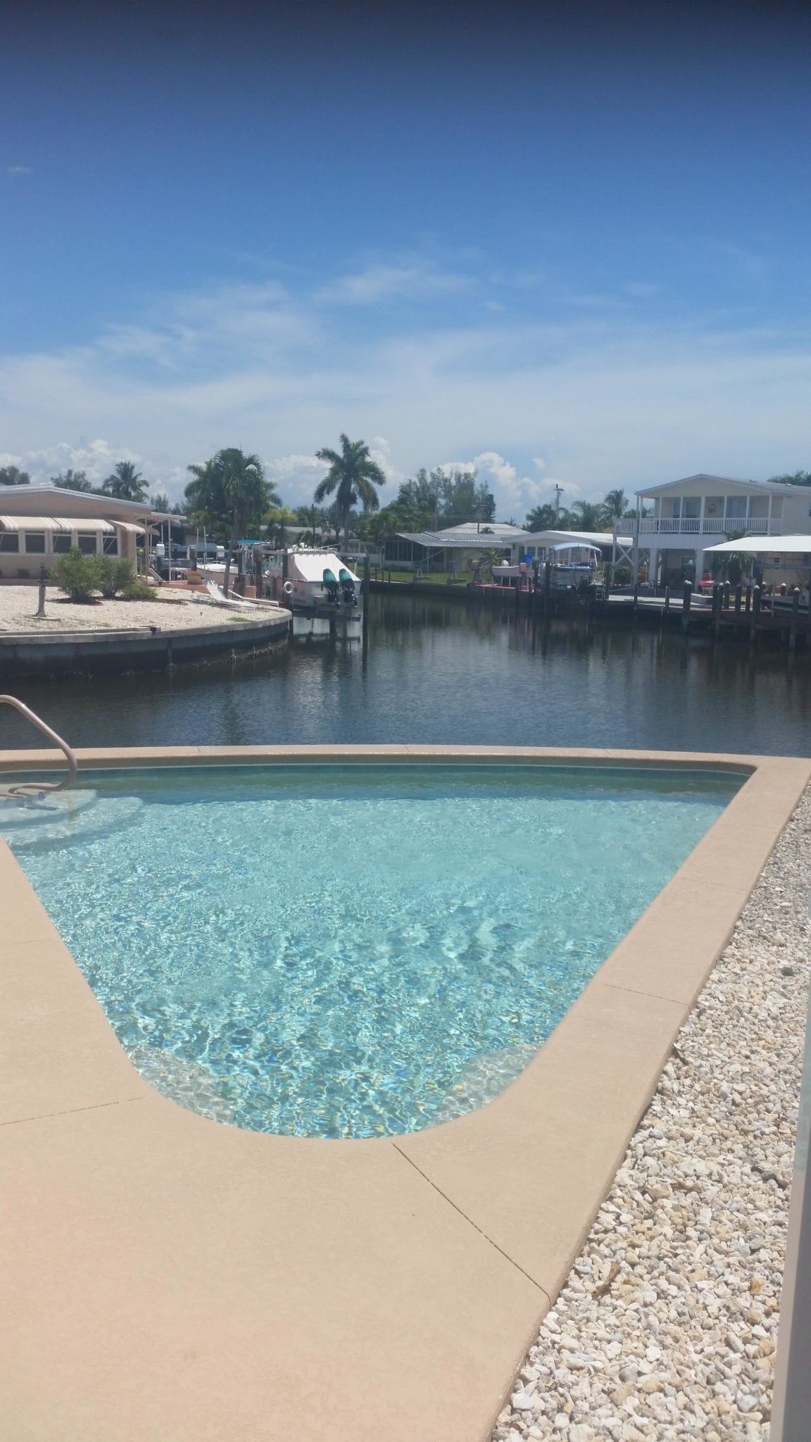 Swimming pool overlooking a canal with houses, boats, and a blue sky.