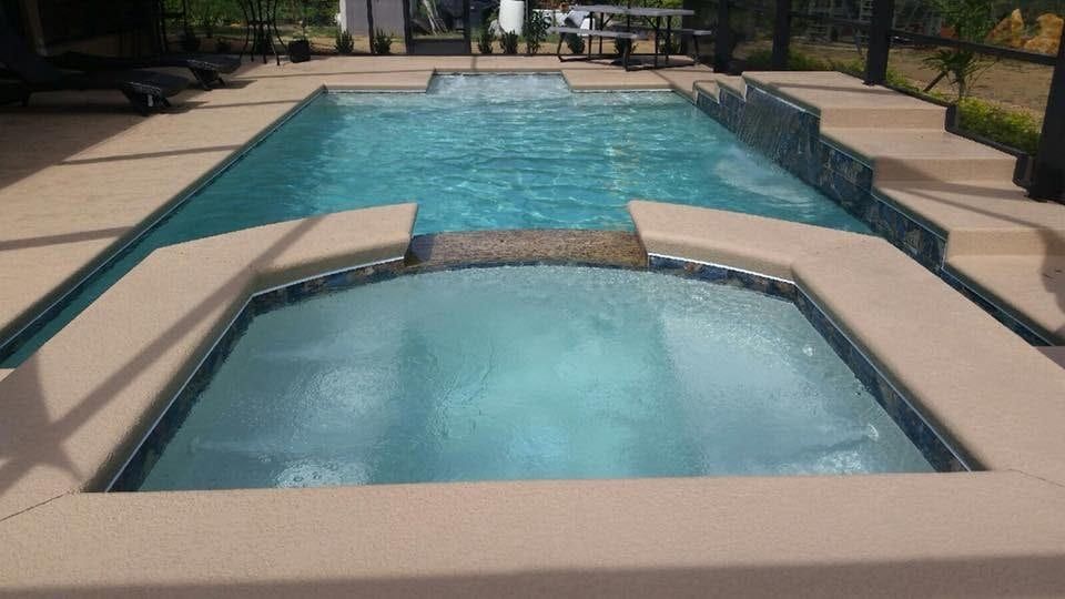 Swimming pool and jacuzzi in outdoor setting with beige decking.