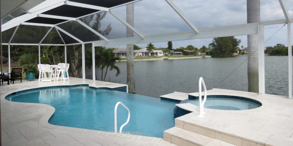 Pool and jacuzzi overlooking a body of water, enclosed by a screened patio.