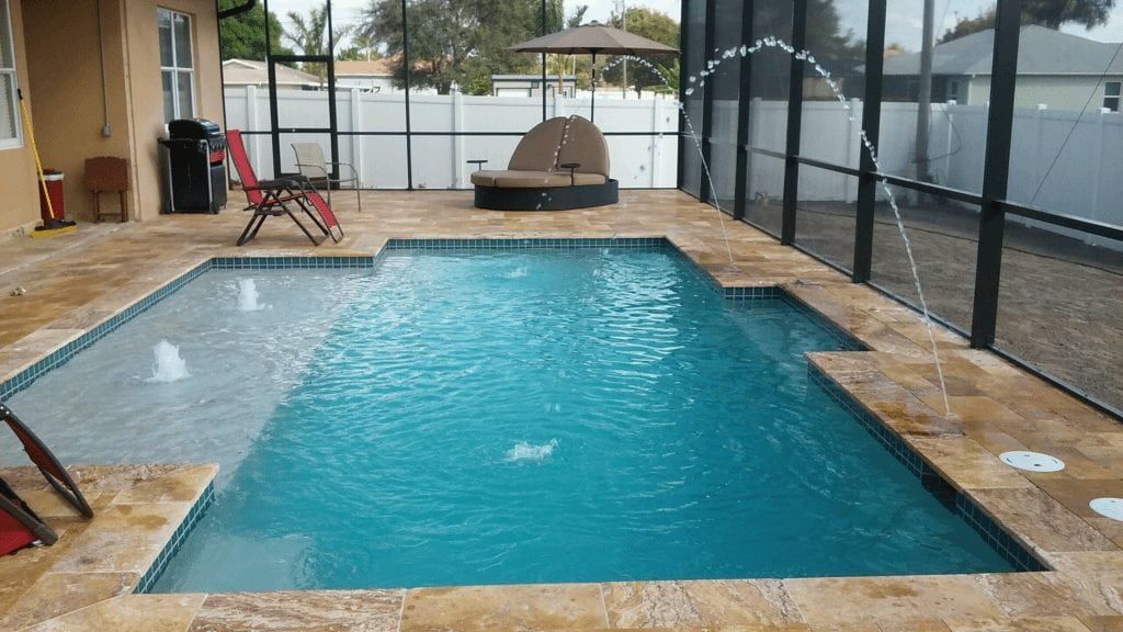 A rectangular swimming pool with fountains, surrounded by a paved patio and screened enclosure.