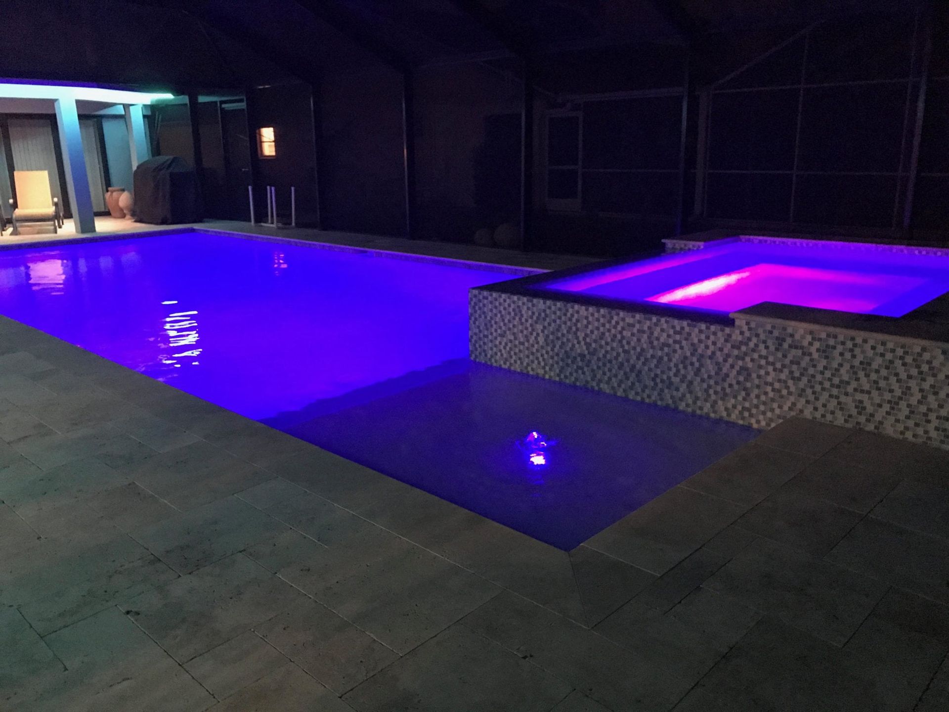 Indoor pool and hot tub with blue and purple lighting.