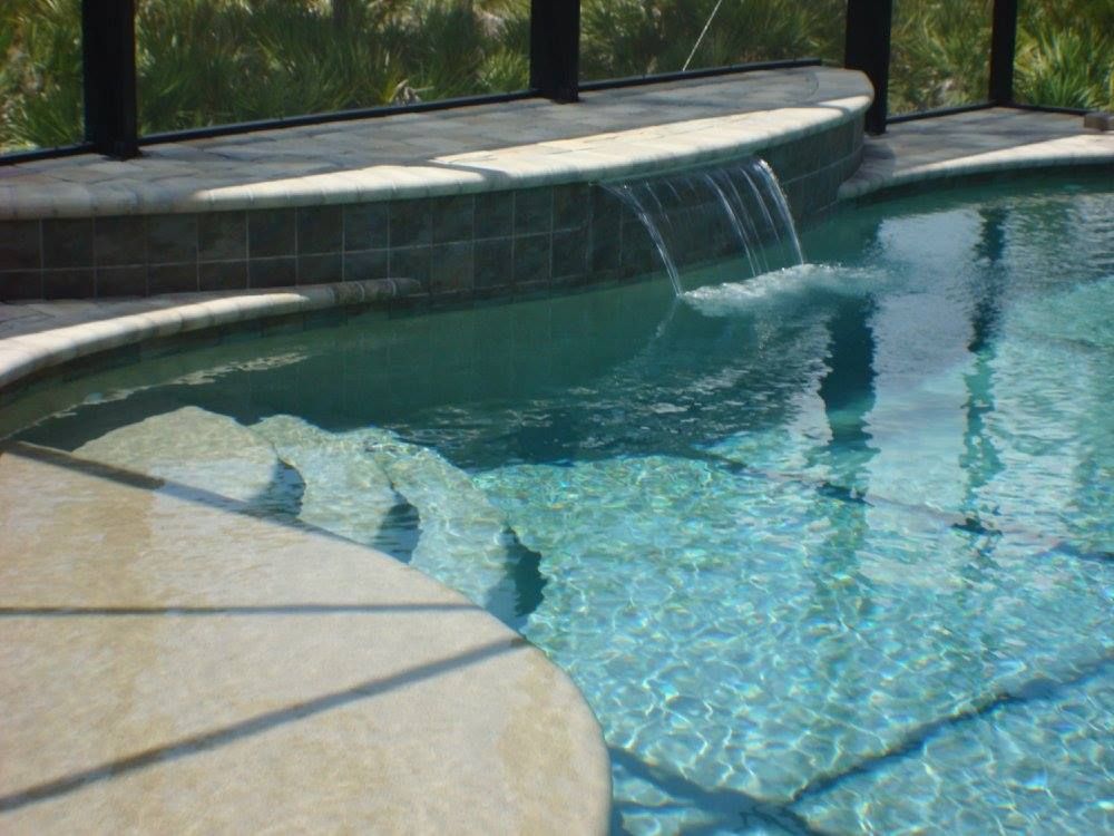 Pool with cascading waterfall and built-in steps; clear blue water reflects sunlight.
