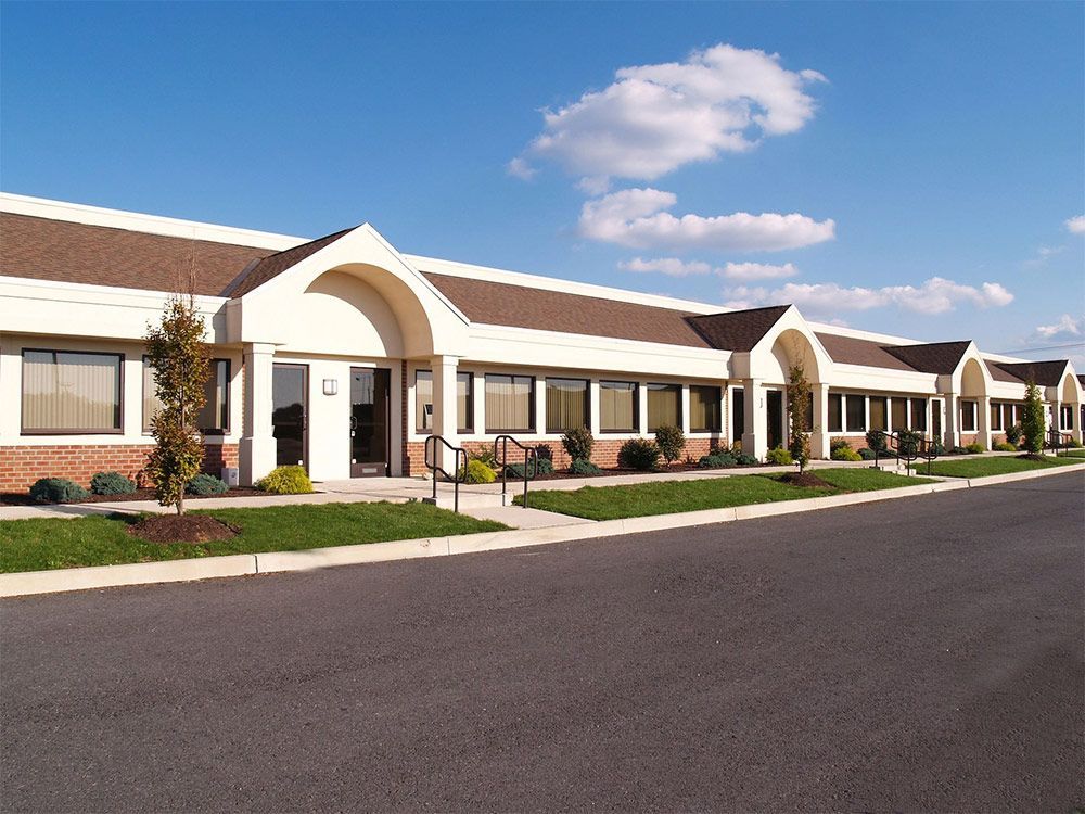 Office building with arched entryways, brick detailing, and green lawn on a sunny day.
