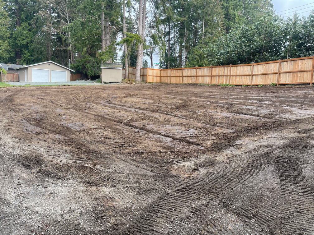 A dirt field with a wooden fence and a garage in the background.