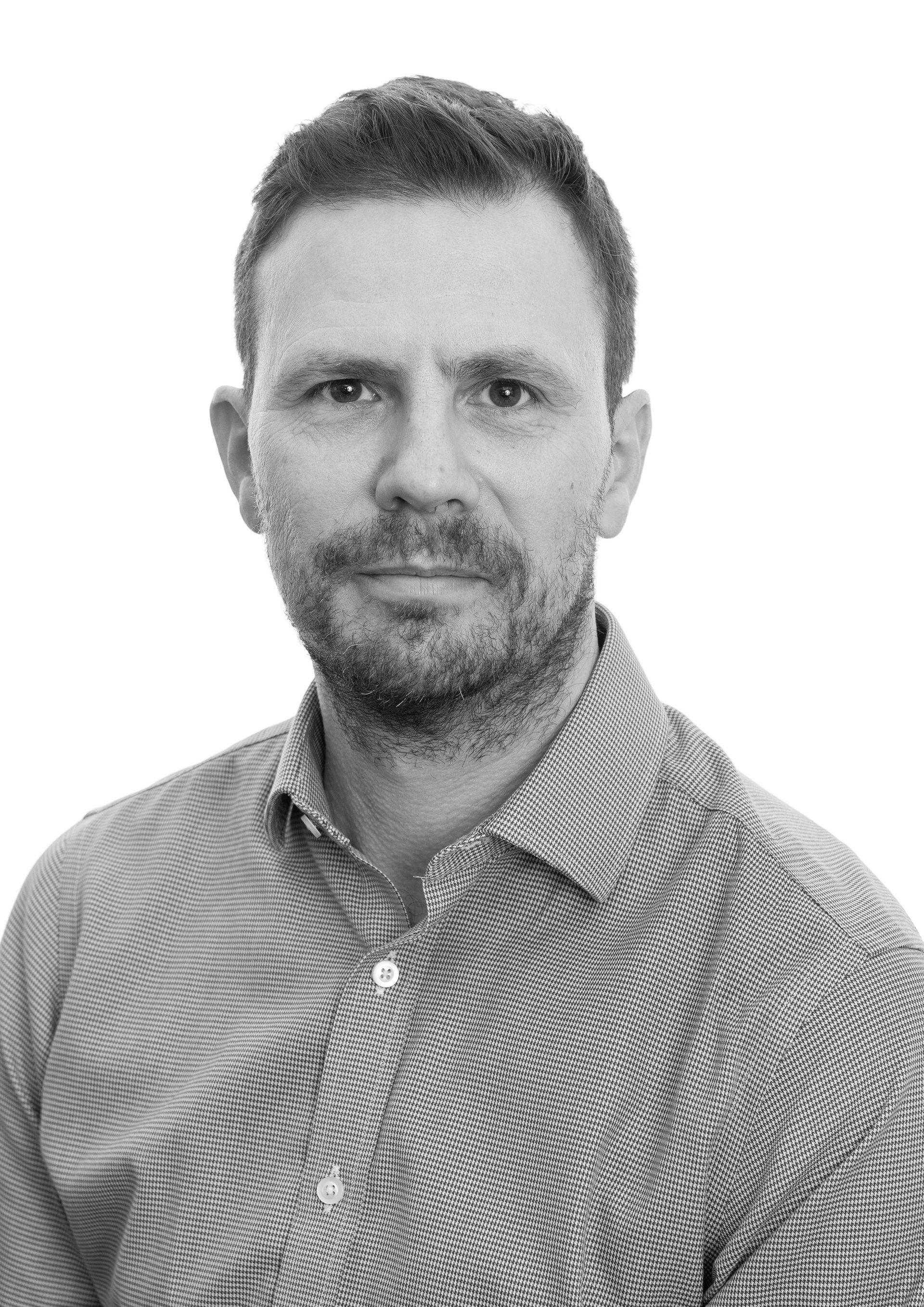 A black and white photo of a man with a beard wearing a plaid shirt.