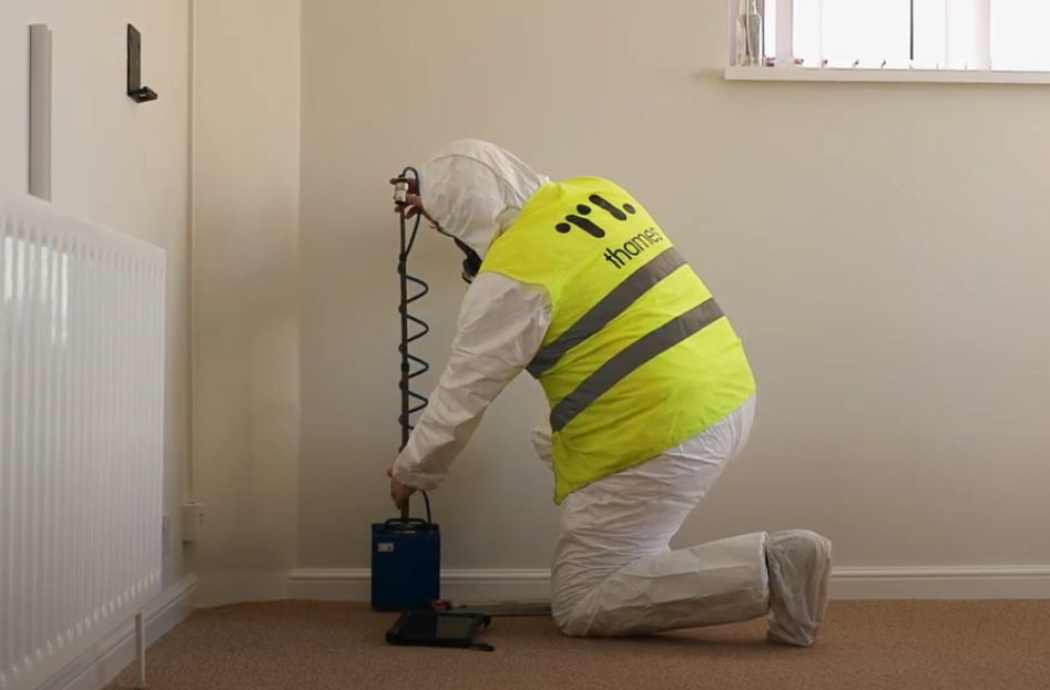 A man in a yellow hi-vis vest is kneeling down in a room with some air testing equipment.