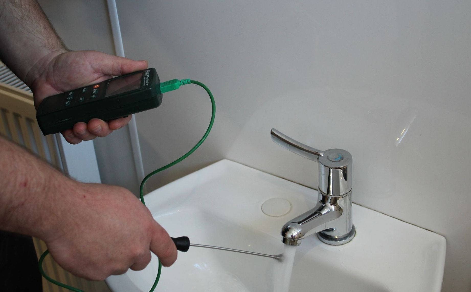 A person is using a thermometer to check the temperature of a sink faucet.