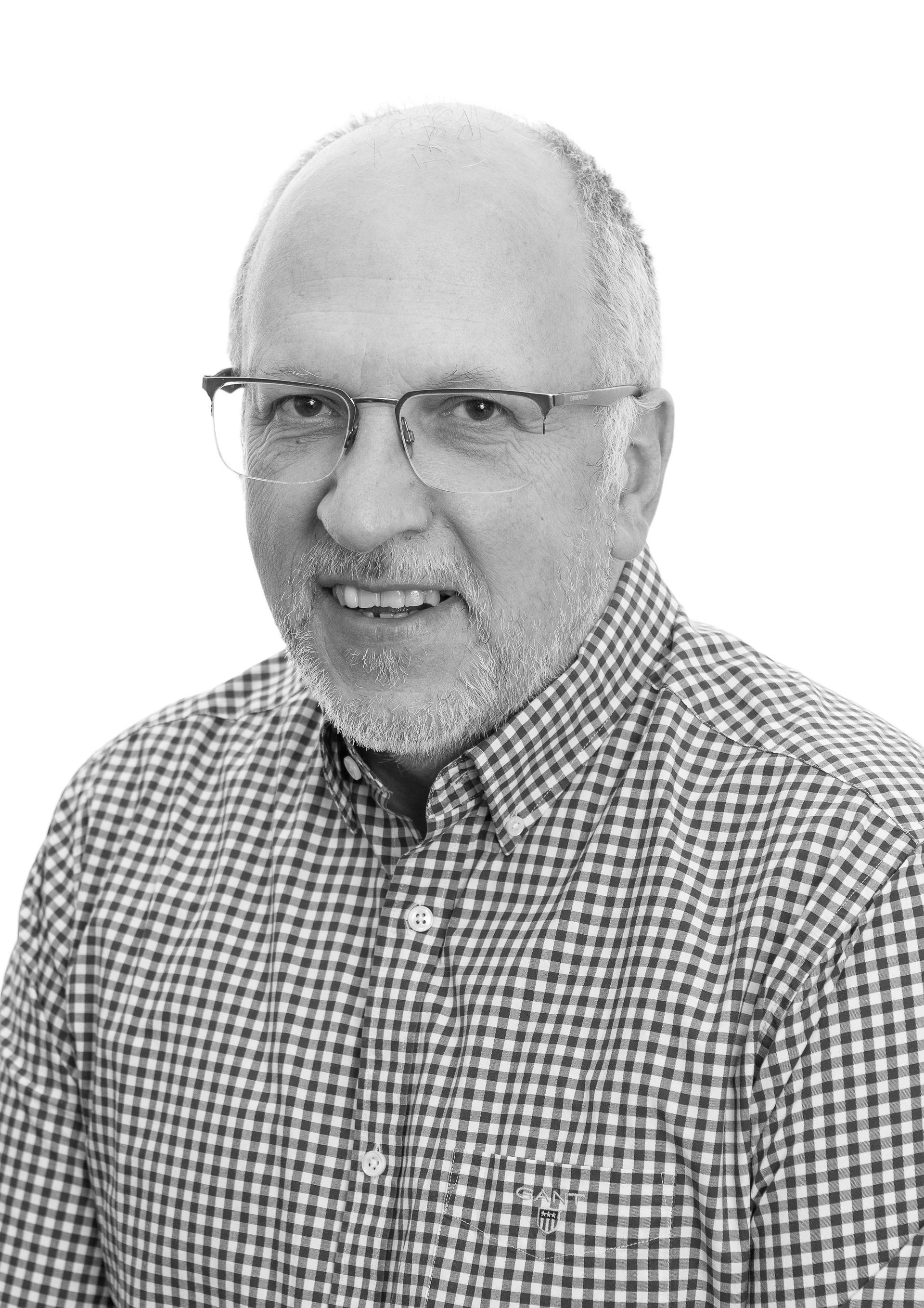 A black and white photo of a man wearing glasses and a plaid shirt.