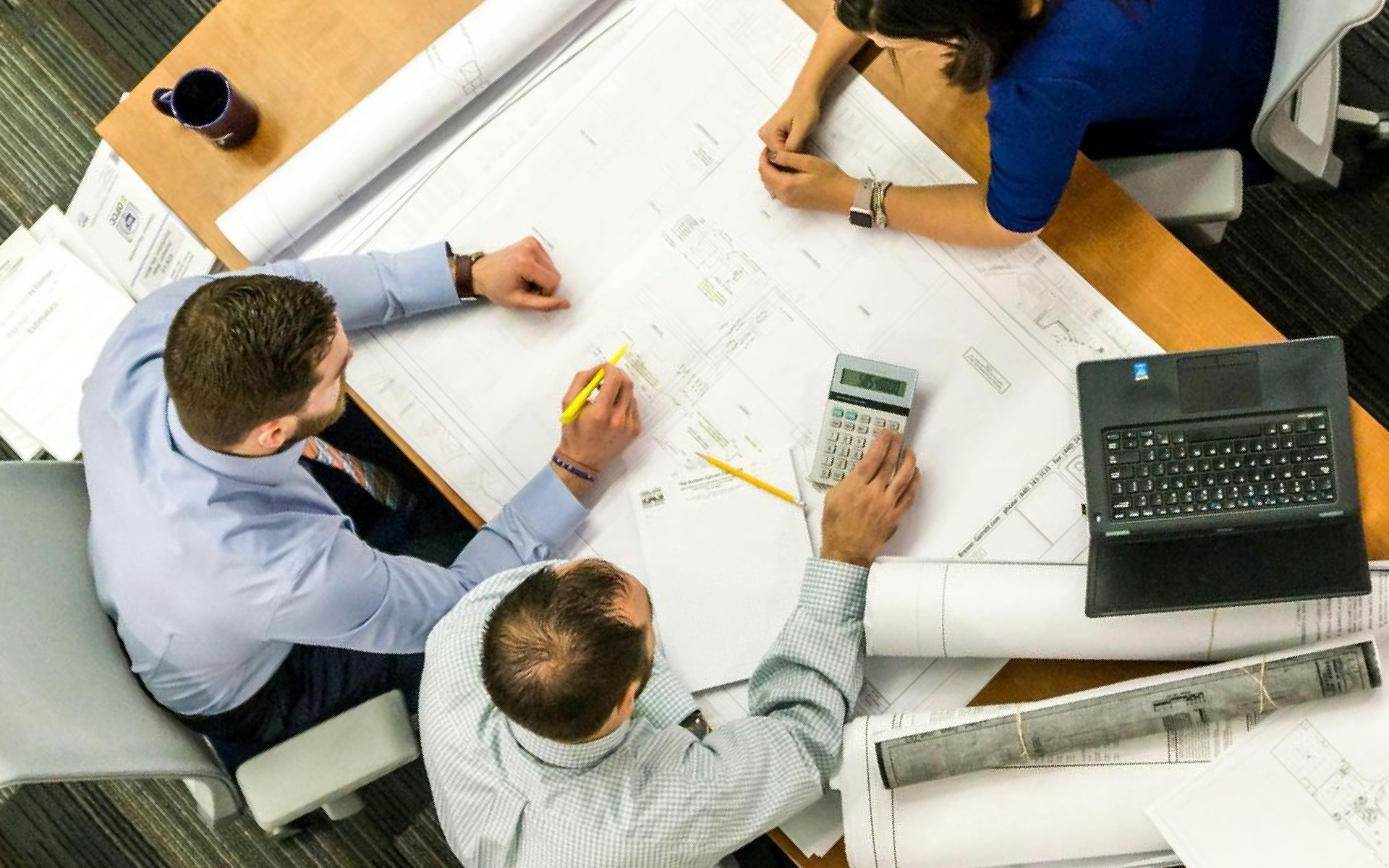 A group of people are sitting around a table looking at blueprints.