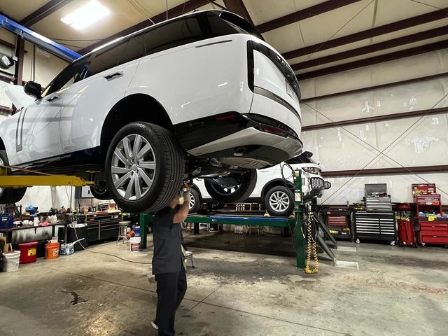 A man is working on a white suv on a lift in a garage.