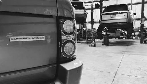 A black and white photo of a range rover on a lift in a garage.
