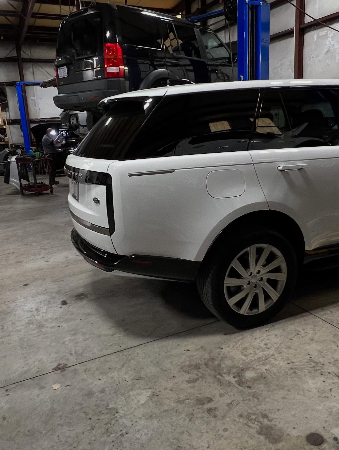 White Range Rover SUV in a repair shop, other vehicles in the background.