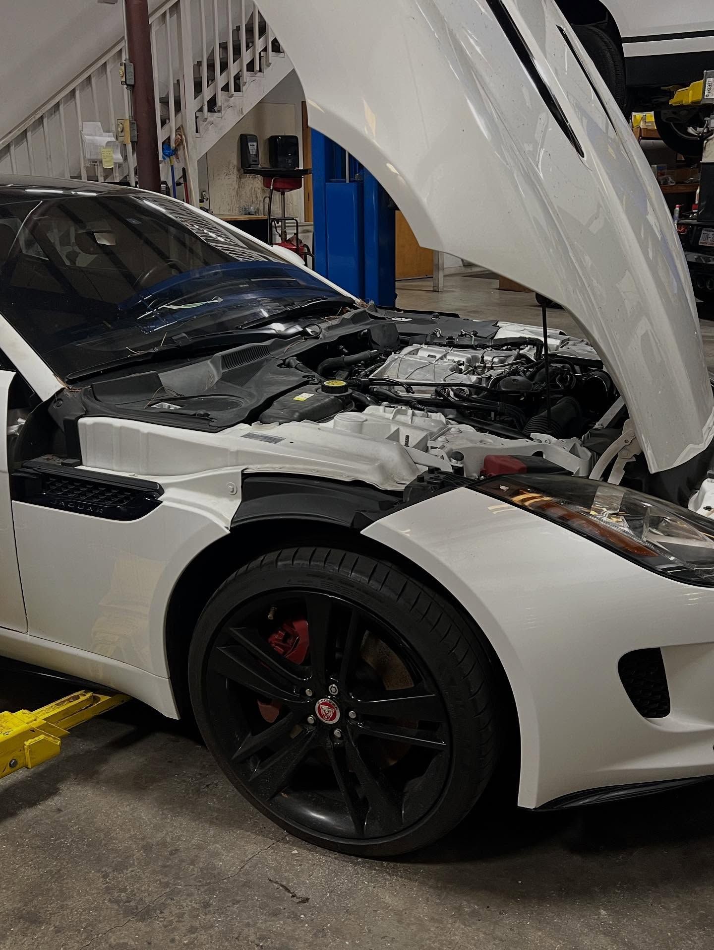White Jaguar F-Type with hood open, parked in a garage. Black wheels, red brake calipers.