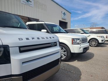 A row of land rover defenders are parked in front of a building.