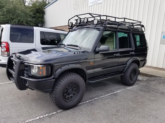A black land rover discovery with a roof rack is parked in a parking lot.