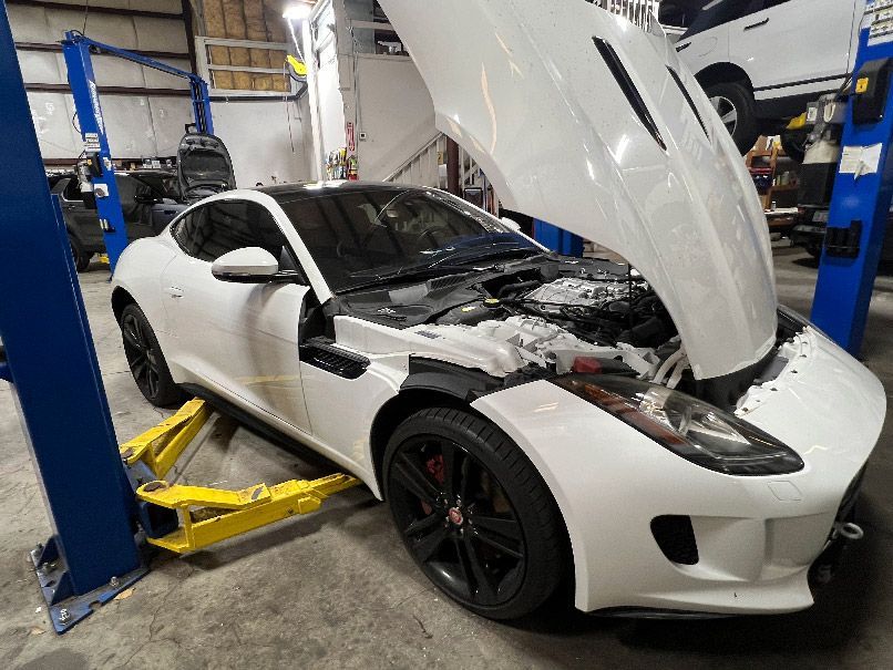 White sports car on a lift in an auto shop with its hood open and front end damaged in New Hanover County, NC