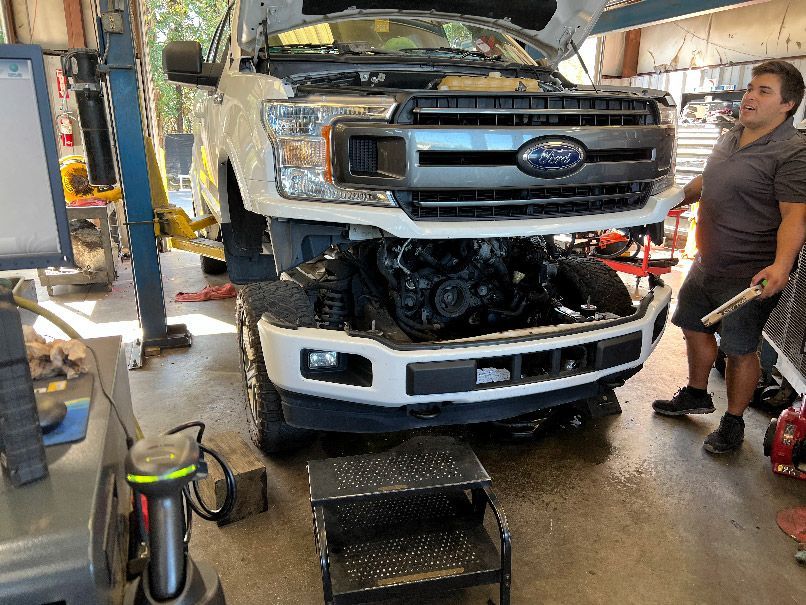 Ford truck front end removed in an auto repair shop, with a mechanic standing beside it in New Hanover County, NC