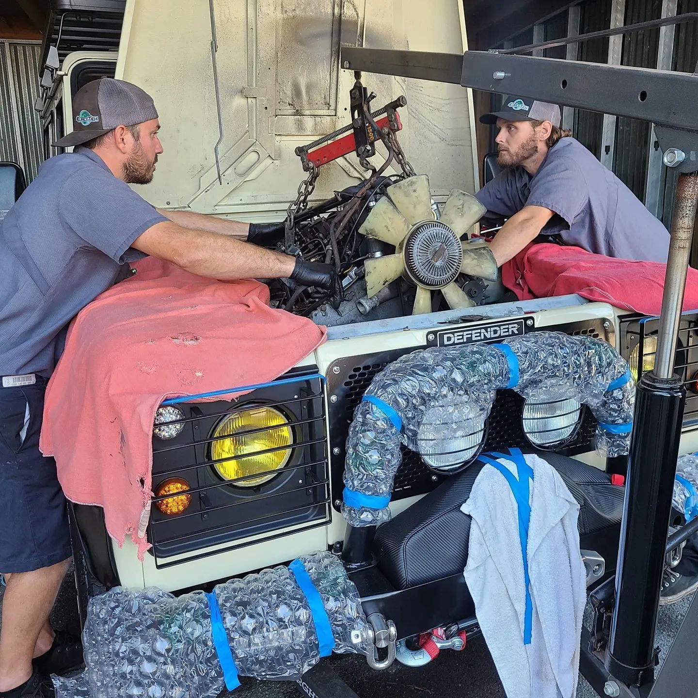 Two men are working on the engine of a jeep.