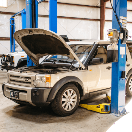 A man is working on a car in a garage with the hood open.