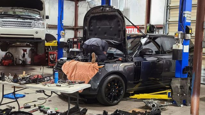 A man is working on a car in a garage with the hood open.