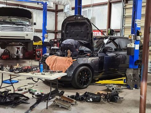 A man is working on a car in a garage with the hood open.