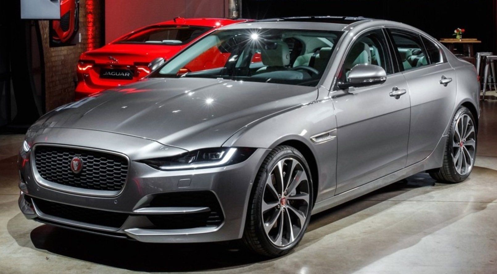 A gray jaguar car is parked in a garage next to a red car.